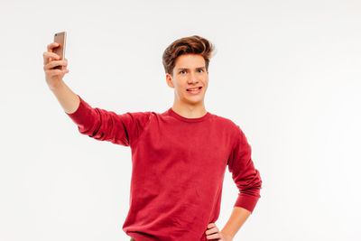 Portrait of smiling young man using phone against white background