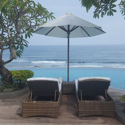 Lounge chairs by swimming pool at beach against sky