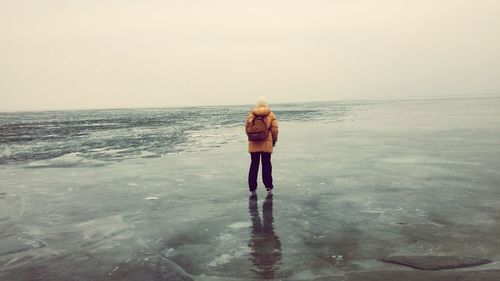 Rear view of man standing on beach against clear sky