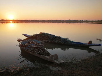 Driftwood on lakeshore against sky during sunset