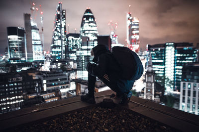 Rear view of man on illuminated cityscape against sky at night