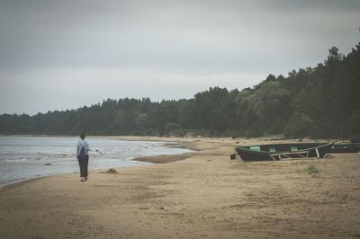 Rear view of woman walking on shore at beach against sky