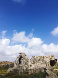 Hiker standing on rock formation against blue sky