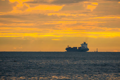 Ship sailing on sea against orange sky