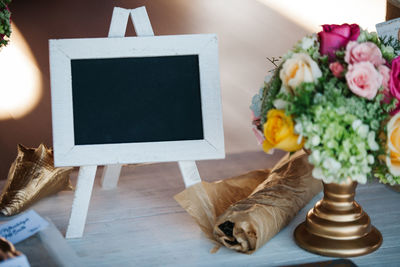 Close-up of flowers by blank picture frame on table