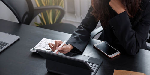 Midsection of woman using mobile phone while sitting on table