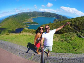 Portrait of happy couple taking selfie while standing on retaining wall against lagoa do fogo