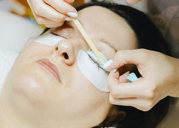 Girl cosmetologist laminates and paints woman eyelashes