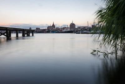 View of river by town against sky during sunset