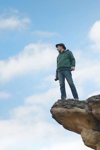 Low angle view of man standing on rock against sky