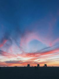 Silhouette people on land against dramatic sky during sunset