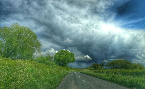 Road passing through field against cloudy sky