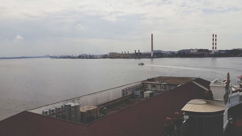 Panoramic view of factory by sea against sky