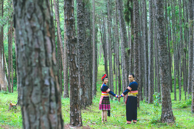 Man and woman standing by tree trunk in forest