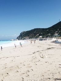People on beach against clear blue sky