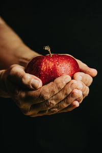 Close-up of hand holding apple over black background