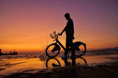 Man riding bicycle on beach against sky during sunset