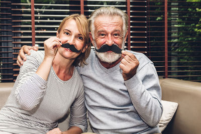 Portrait of couple wearing artificial mustache at home