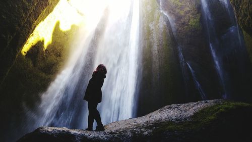 Low angle view of woman standing on rock against waterfall