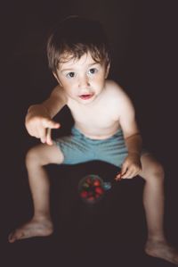 Portrait of cute boy sitting against black background