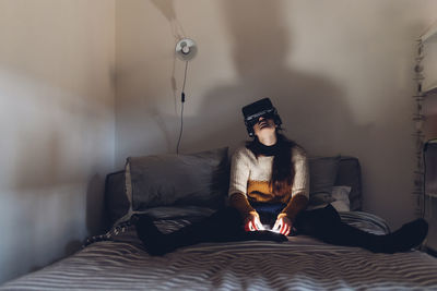 Woman with virtual reality headset sitting on bed at home