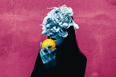 Close-up of hand holding rose against wall