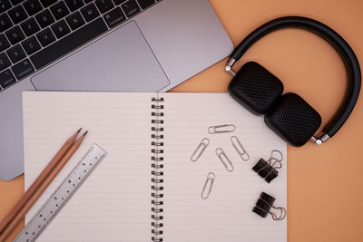 Directly above shot of laptop with office supplies and headphones on brown background