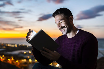 Man holding smart phone against sky during sunset