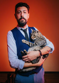 Portrait of young man holding dog against orange background