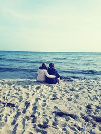 Rear view of couple sitting on beach against clear sky
