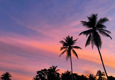 Low angle view of silhouette palm trees against cloudy sky during sunset
