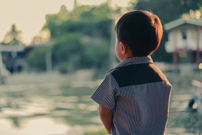 Rear view of boy standing against lake during sunset