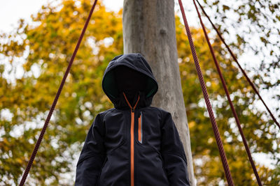 Low angle view of boy wearing hooded shirt against pole
