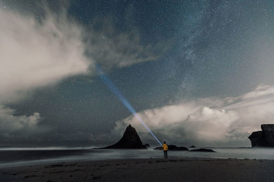 Rear view of man holding flashlight while standing at beach