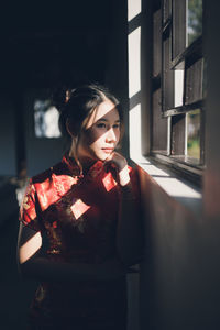 Young woman looking away while standing by window