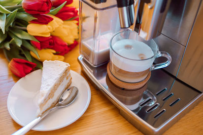 Cup of coffee with milk, piece of cake and tulips flowers on wooden kitchen table. freshly brewed 
