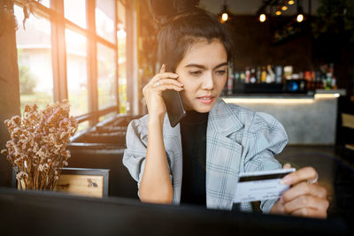 Young woman answering mobile phone while looking at credit card