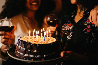 Midsection of women with birthday cake in darkroom