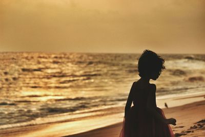 Girl standing at beach against sky during sunset