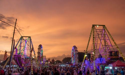 People at amusement park against sky during sunset