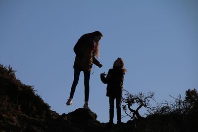 Low angle view of siblings standing on rocks against clear sky