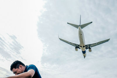 Low angle view of man below airplane flying against sky