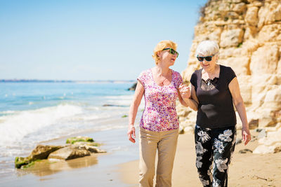 Two elderly women are walking along the rocky shore