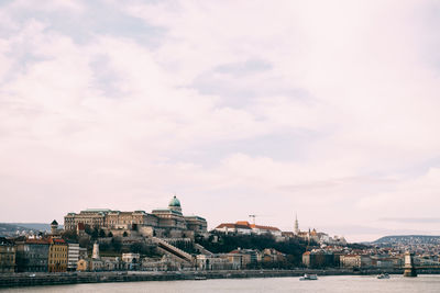 Buildings at waterfront against cloudy sky