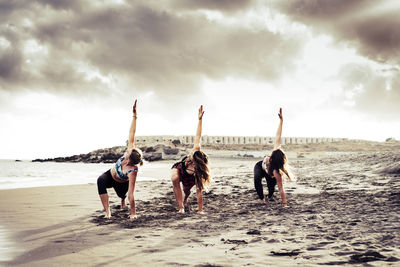 Women doing stretching at beach against sky suring sunset