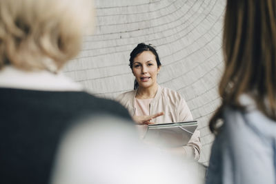 Businesswoman discussing with female coworkers against wall at office