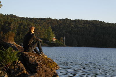 Man sitting on rock looking at waterfall against sky