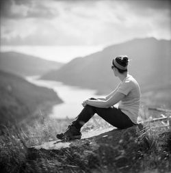 Side view of woman sitting on rock at cliff against valley