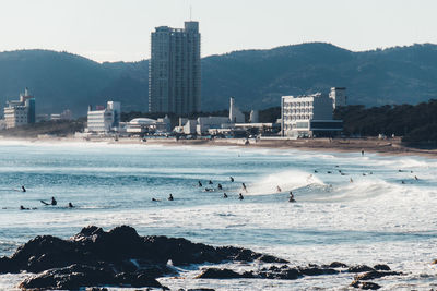 People surfing on sea against mountains during sunny day