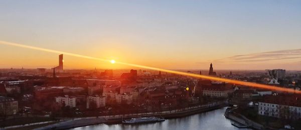 Bridge over river amidst buildings in city against sky during sunset